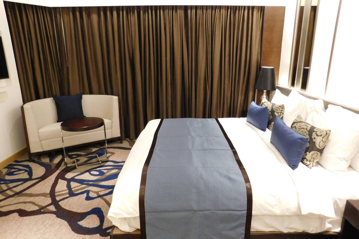 A hotel room with a bed, a sofa, a small round table, and a large window with curtains.