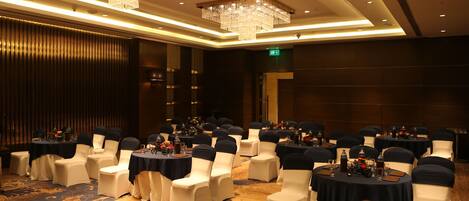 A conference room with round tables, white chairs, and chandeliers.