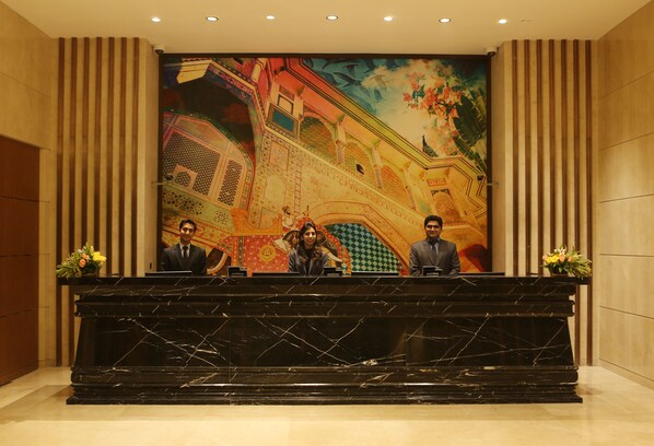 Un mostrador de recepción con encimera de mármol, flanqueado por paneles verticales de madera y un gran mural que representa un edificio tradicional.