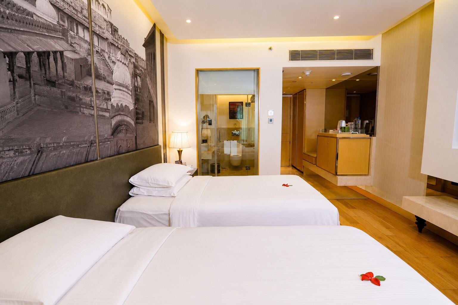 A hotel room with two beds, a large mural, a bathroom with a glass shower, and a kitchenette.
