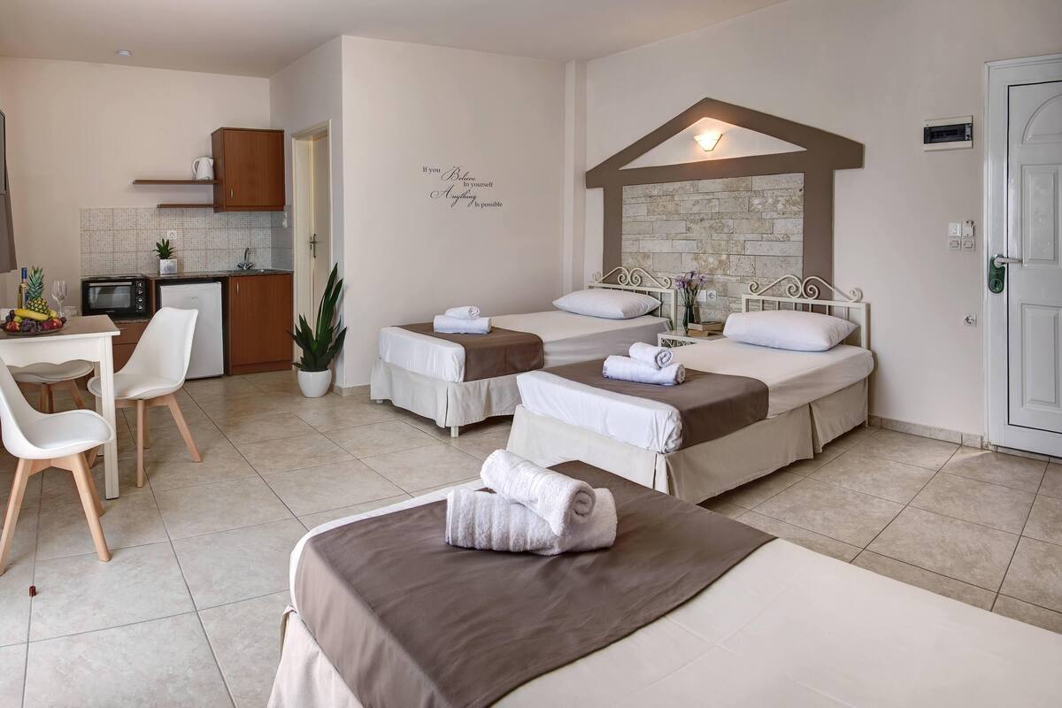A hotel room with two beds, a small kitchenette, a dining area with a table and chairs, and a decorative wall with a motivational quote.