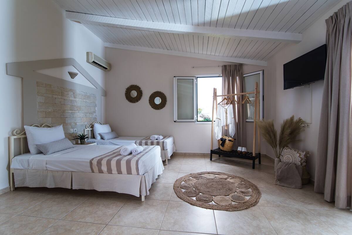 A bedroom with two beds, a flat-screen TV, a large window with curtains, and a decorative wall piece.