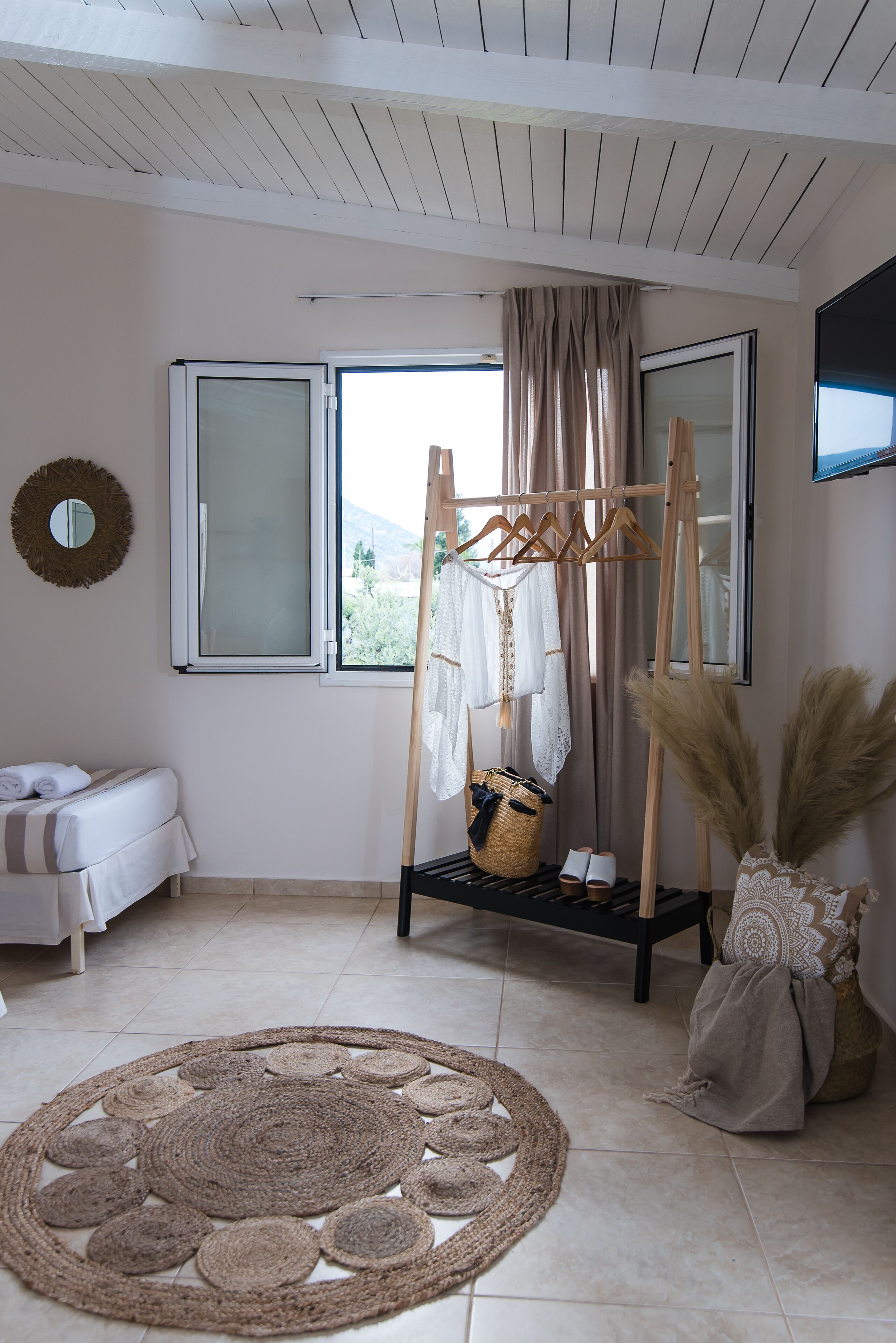 Una habitación con cama, un tendedero, una ventana con cortinas, un espejo y una alfombra grande de tejido.