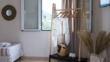 Una habitación con cama, un tendedero, una ventana con cortinas, un espejo y una alfombra grande de tejido.