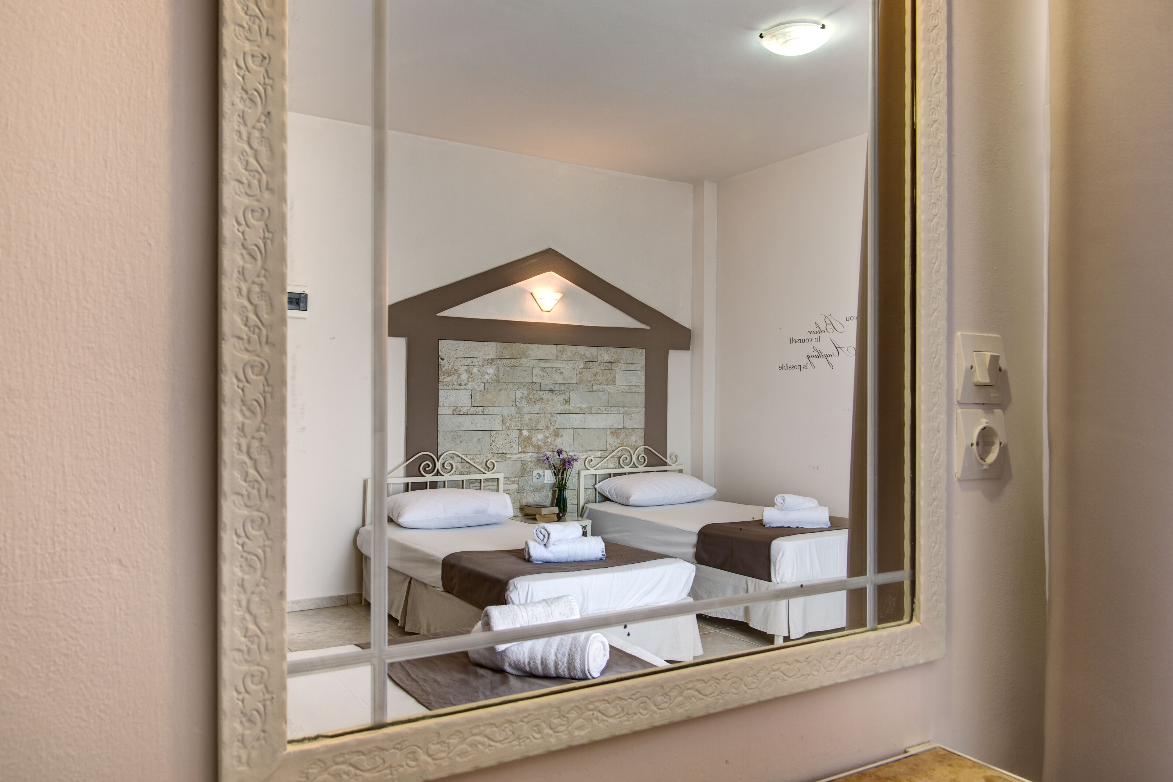 Habitación de hotel con un espejo grande, una pared decorativa de piedra y dos camas con ropa blanca.