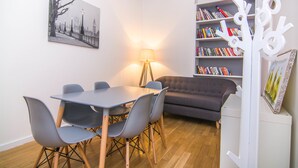 Ein Zimmer mit Esstisch, Stühlen, einer Couch, einem Bücherregal und einer Lampe.