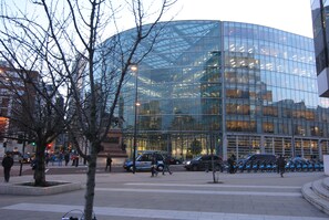 A modern glass building with a curved facade, surrounded by a plaza with trees and parked vehicles. - Apartment Wharf – Vintage Central London Apartment (London)