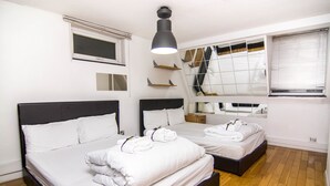 Ein Hotelzimmer mit zwei Betten, Holzboden, einer Deckenleuchte, einem Fenster mit Jalousien und einem Spiegel an der Wand.