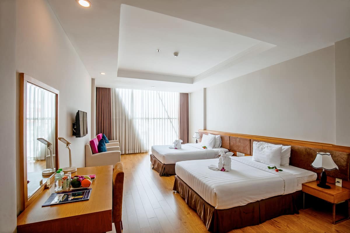 A hotel room with two beds, a desk with a chair, a lamp, and a TV on the wall.