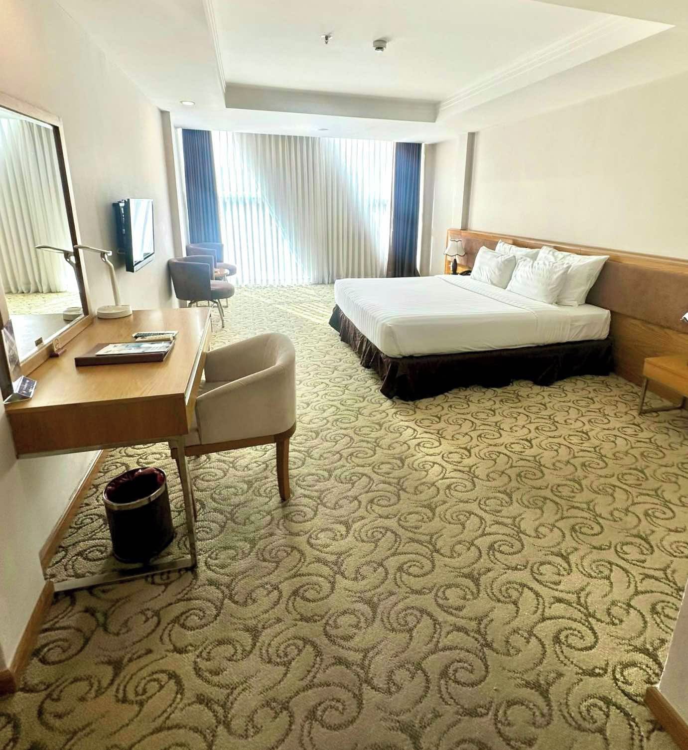 A hotel room with a bed, a desk, a chair, a television, and a window with curtains.