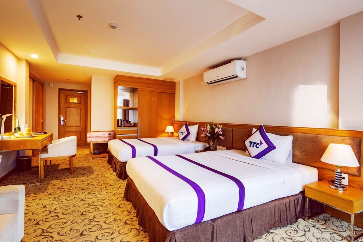 A hotel room with two beds, a desk, a chair, a small table, and a nightstand.