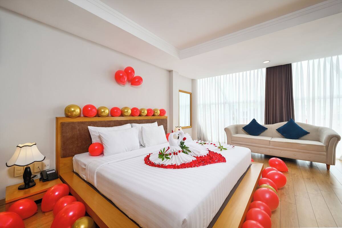A hotel room with a bed, a sofa, a nightstand, and a window with curtains.