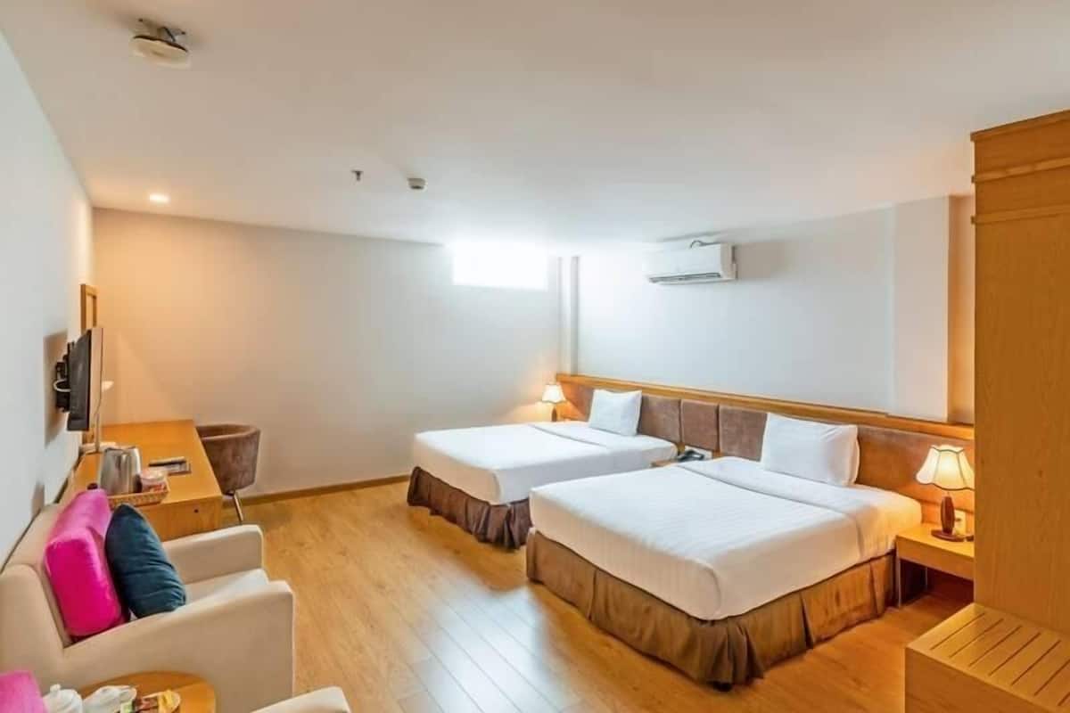 A hotel room with two beds, a sofa, a TV, and a wooden floor.