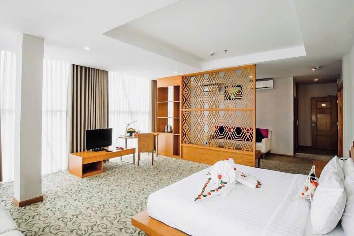 A hotel room with a bed, a desk, a TV, and a decorative partition.