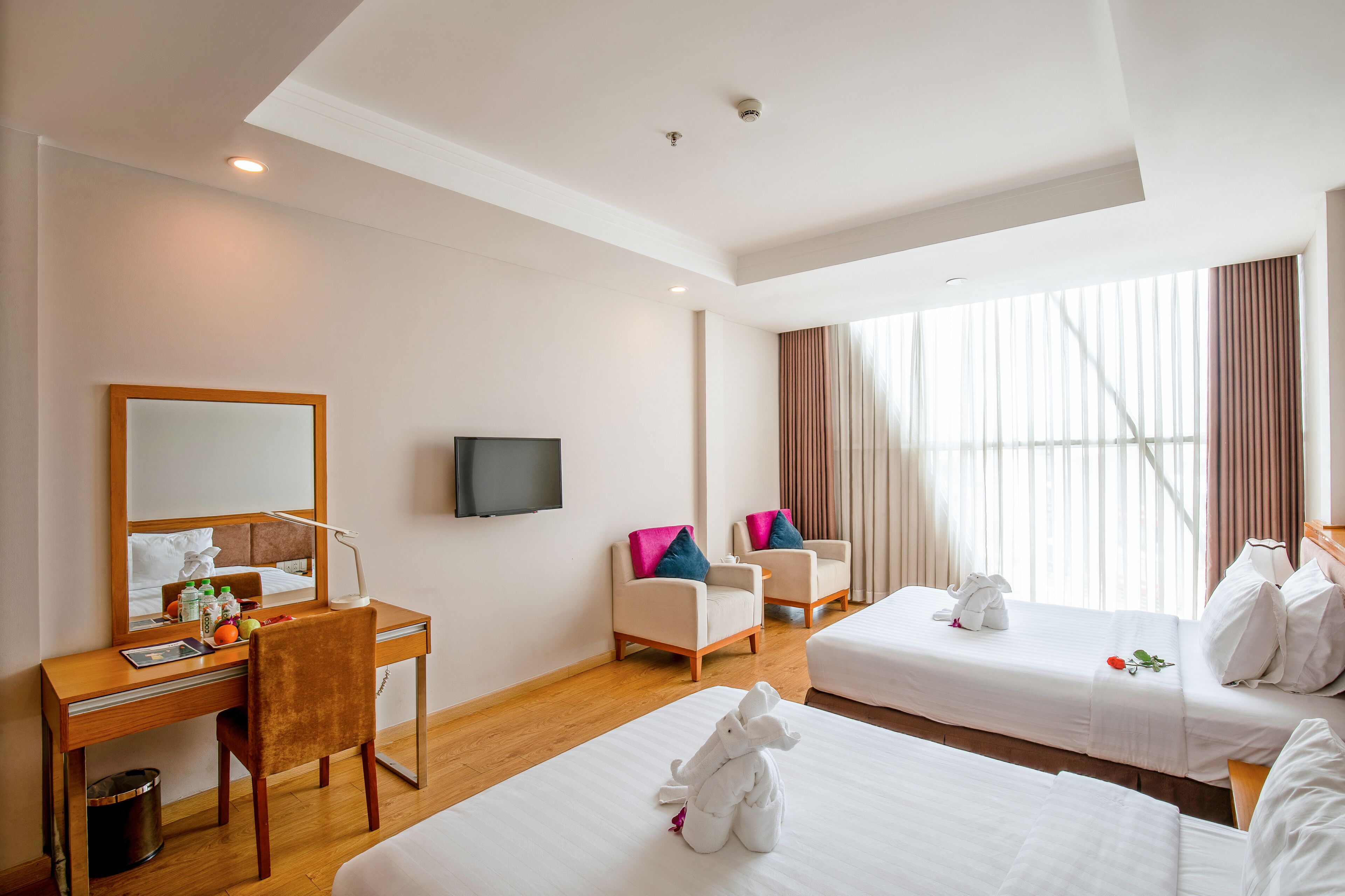 A hotel room with a desk, two chairs, a television, and two beds.
