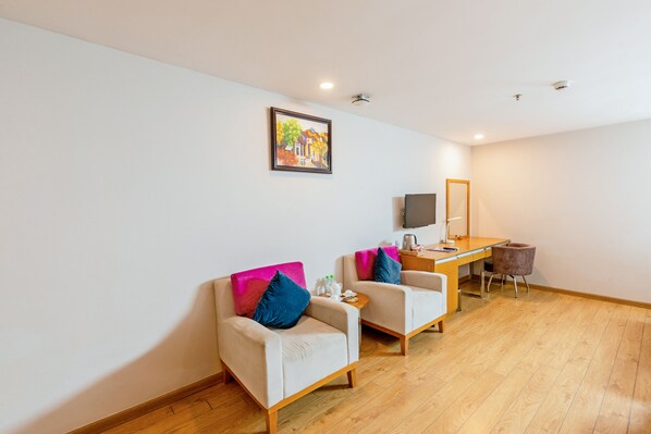 Une chambre moderne avec deux fauteuils, un bureau en bois, un téléviseur à écran plat et un tableau accroché au mur.