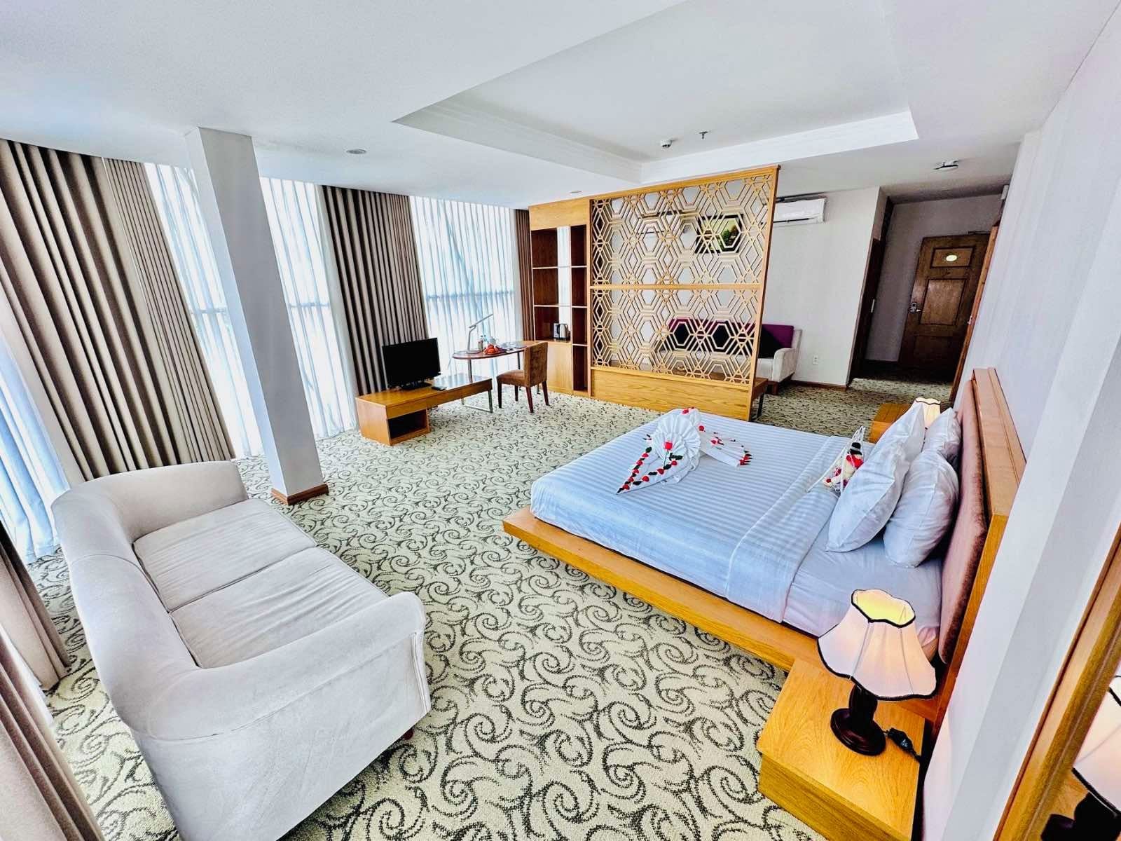A hotel room with a bed, a sofa, a desk with a TV, and a decorative partition.