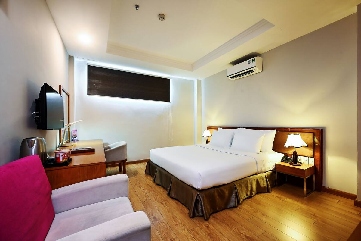 A hotel room with a bed, bedside table, chair, desk, and a TV.