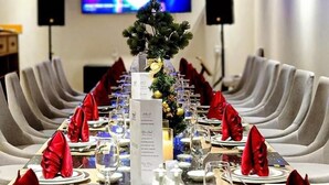 Una mesa de conferencias dispuesta para un evento formal, con un árbol de Navidad como centro de mesa, rodeada de sillas tapizadas en gris.