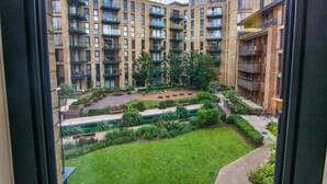 A multi-story residential building with balconies, a central courtyard with benches and greenery, and a view through a window.