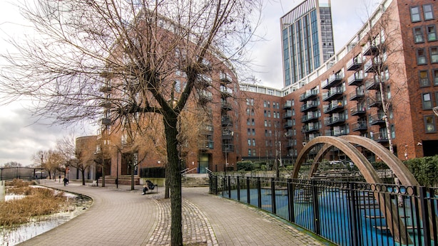 A brick building with multiple balconies, a curved metal fence, and a paved walkway.