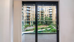 A view from a balcony with a glass door leading to a courtyard with benches and greenery.