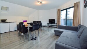 Un salon moderne avec un canapé gris, une table à manger avec des chaises, un téléviseur et un balcon avec des rideaux.