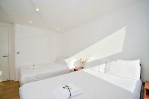 A hotel room with two single beds, a wooden nightstand, a lamp, and a door. - Apartment Wharf – Canary South (London)
