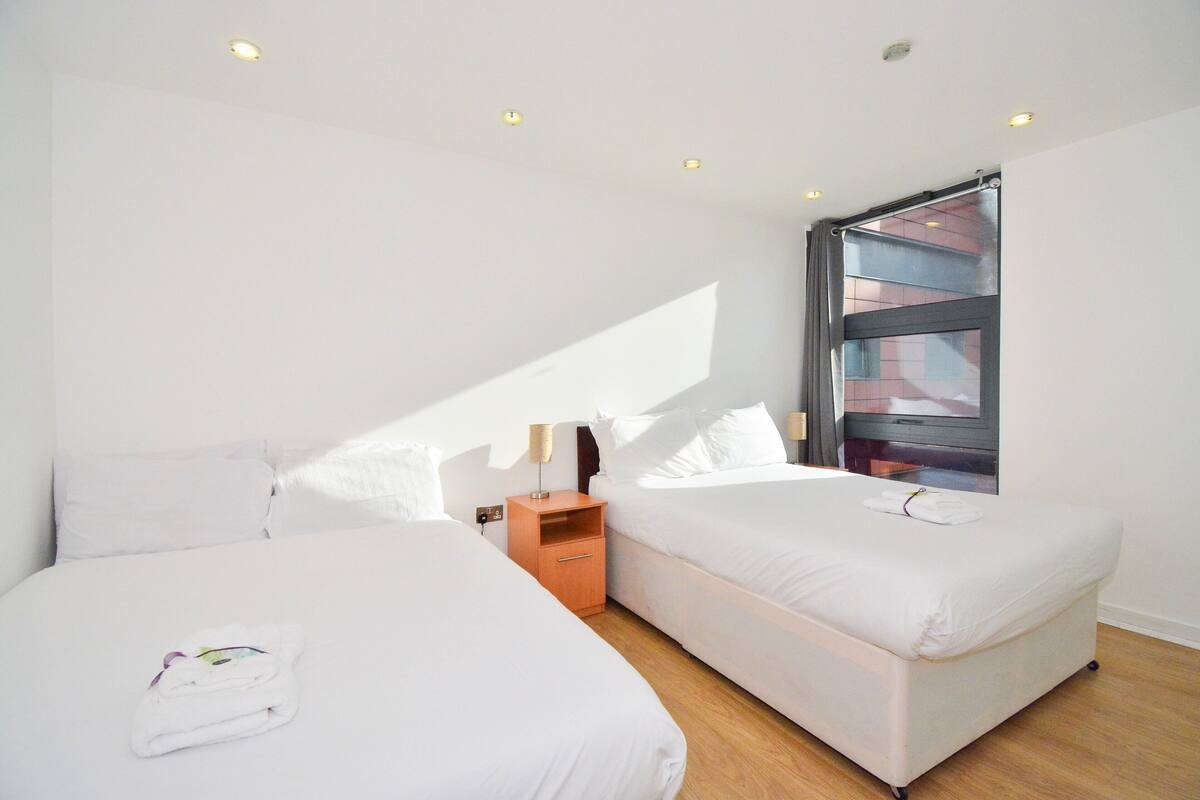Ein Hotelzimmer mit zwei Betten, einem Holfnachtkästchen und einem großen Fenster.