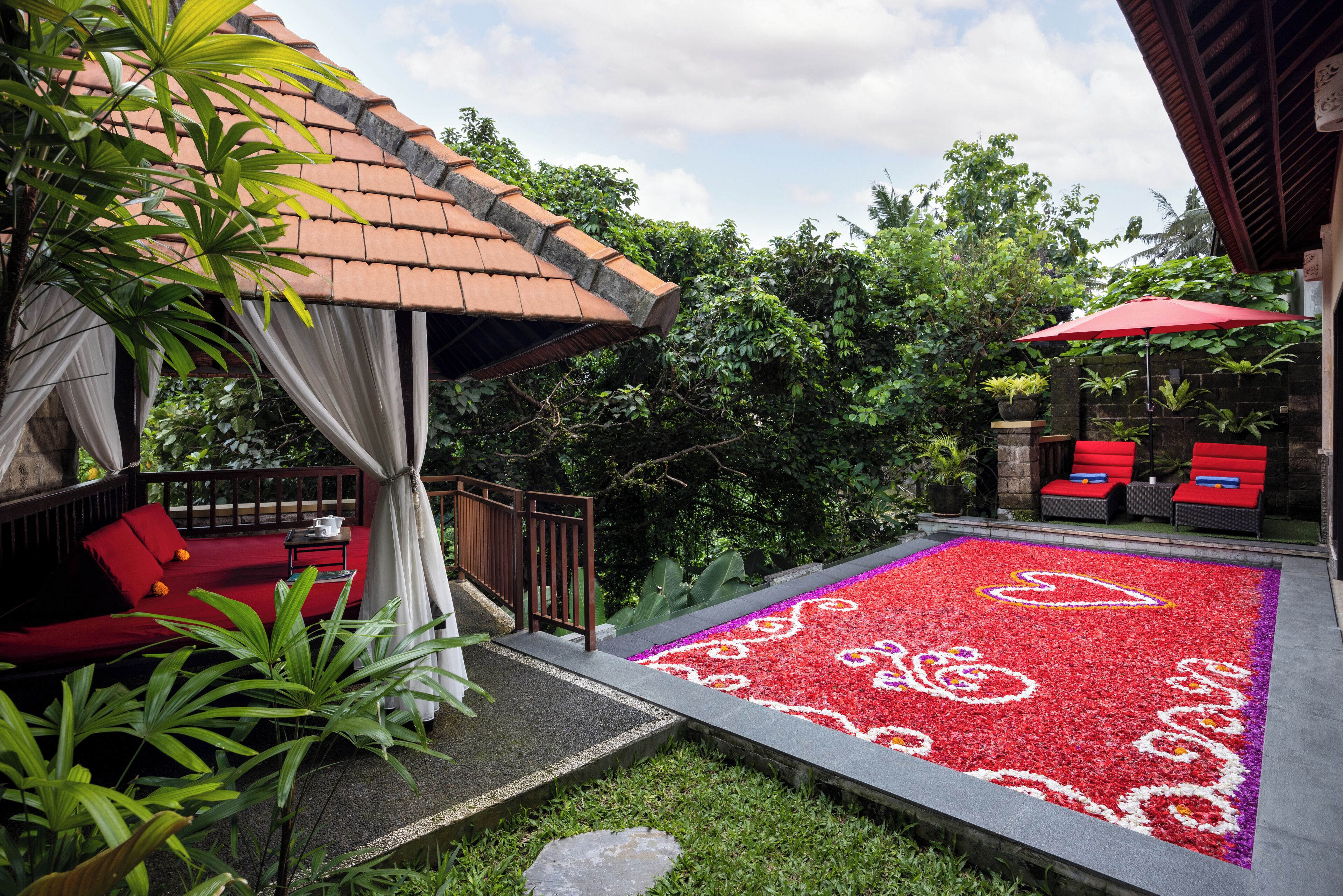 A patio area with a red and white patterned floor, a red sofa, and a red umbrella.