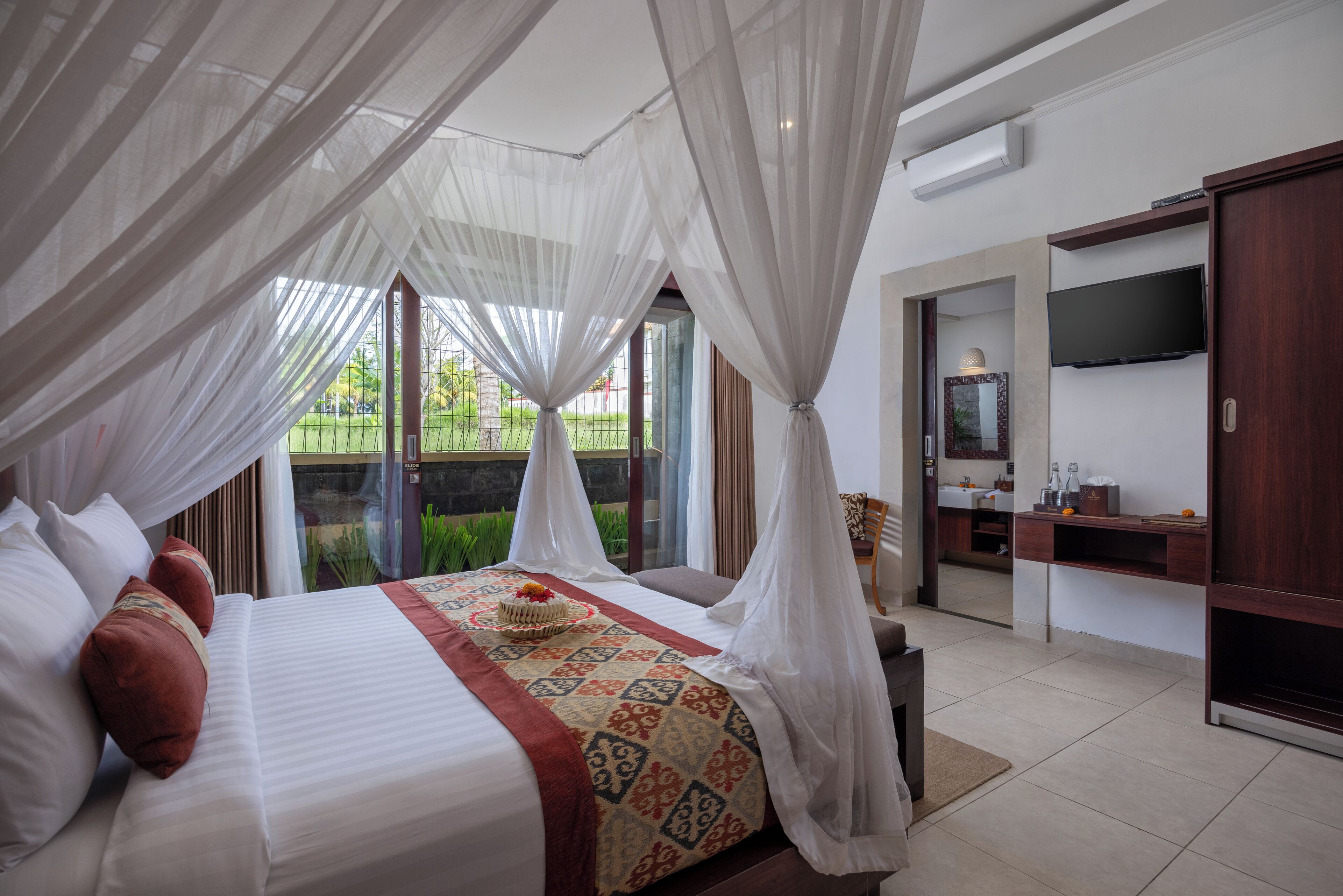 A spacious bedroom with a large bed, a TV, and a view of a garden.