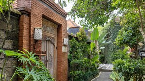 Een smal, met stenen bestraat pad, omzoomd door weelderige begroeiing en een houten poort.