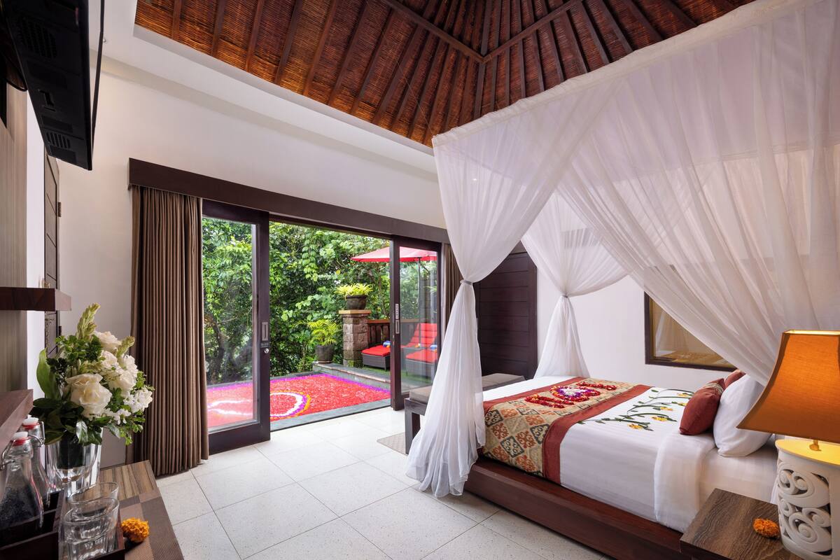 A bedroom with a bed, a bedside table, a nightstand, a window, and a view of the outdoors.