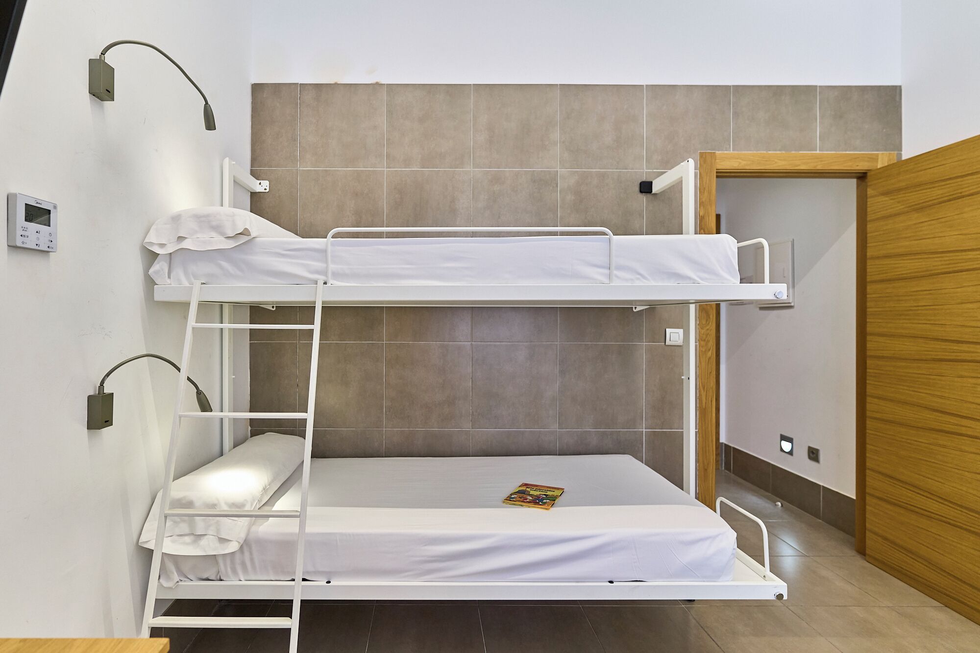 Een slaapkamer met een stapelbed, een tafeltje en een deur.
