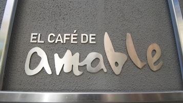 A sign with the text "EL CAFÉ DE Amable" on a textured grey background.