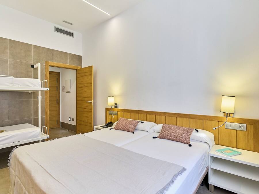 A hotel room with a large bed, a smaller bed, a desk, and a bedside table.