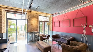 A modern interior with a red accent wall, a glass coffee table, leather sofas, and a brick wall. - The Book Factory Hostel by gaiarooms (Valladolid)