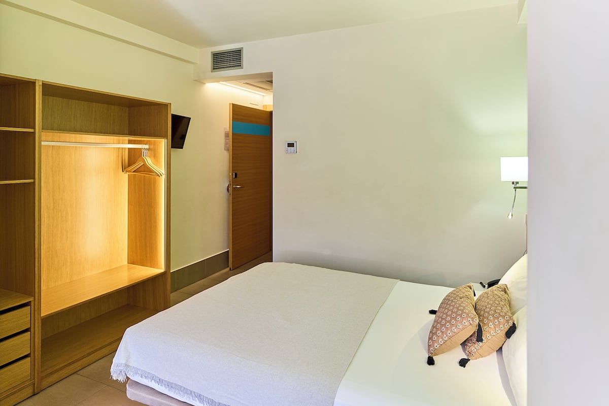 A hotel room with a bed, a wardrobe, a bedside table, and a wall-mounted TV.