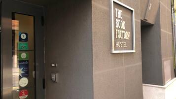 Entrada a un hostal con un letrero que dice 'THE ROOM FACTORY HOSTEL' y varias pegatinas en la puerta.