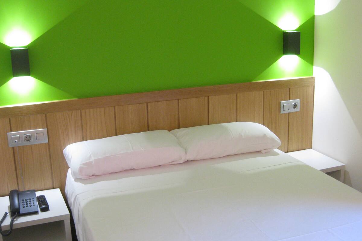 A hotel room with a bed, a bedside table with a phone, and green wall lighting.
