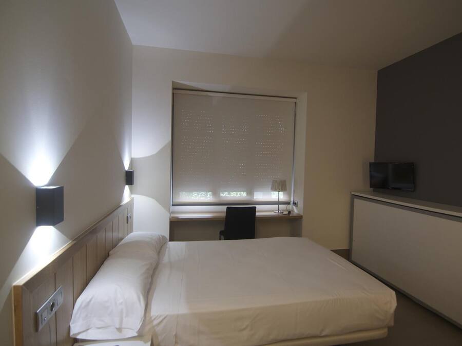 Un dormitorio pequeño y ordenado con una cama individual, un escritorio y un televisor.