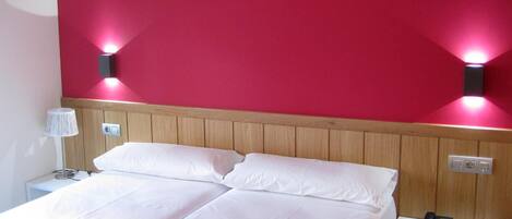 A hotel room with a double bed, a nightstand with a phone and remote, and two wall-mounted lights.