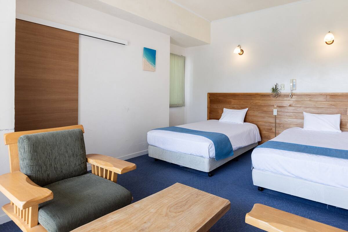 Une chambre d’hôtel avec deux lits, un canapé, une table basse en bois et un luminaire fixé au mur.