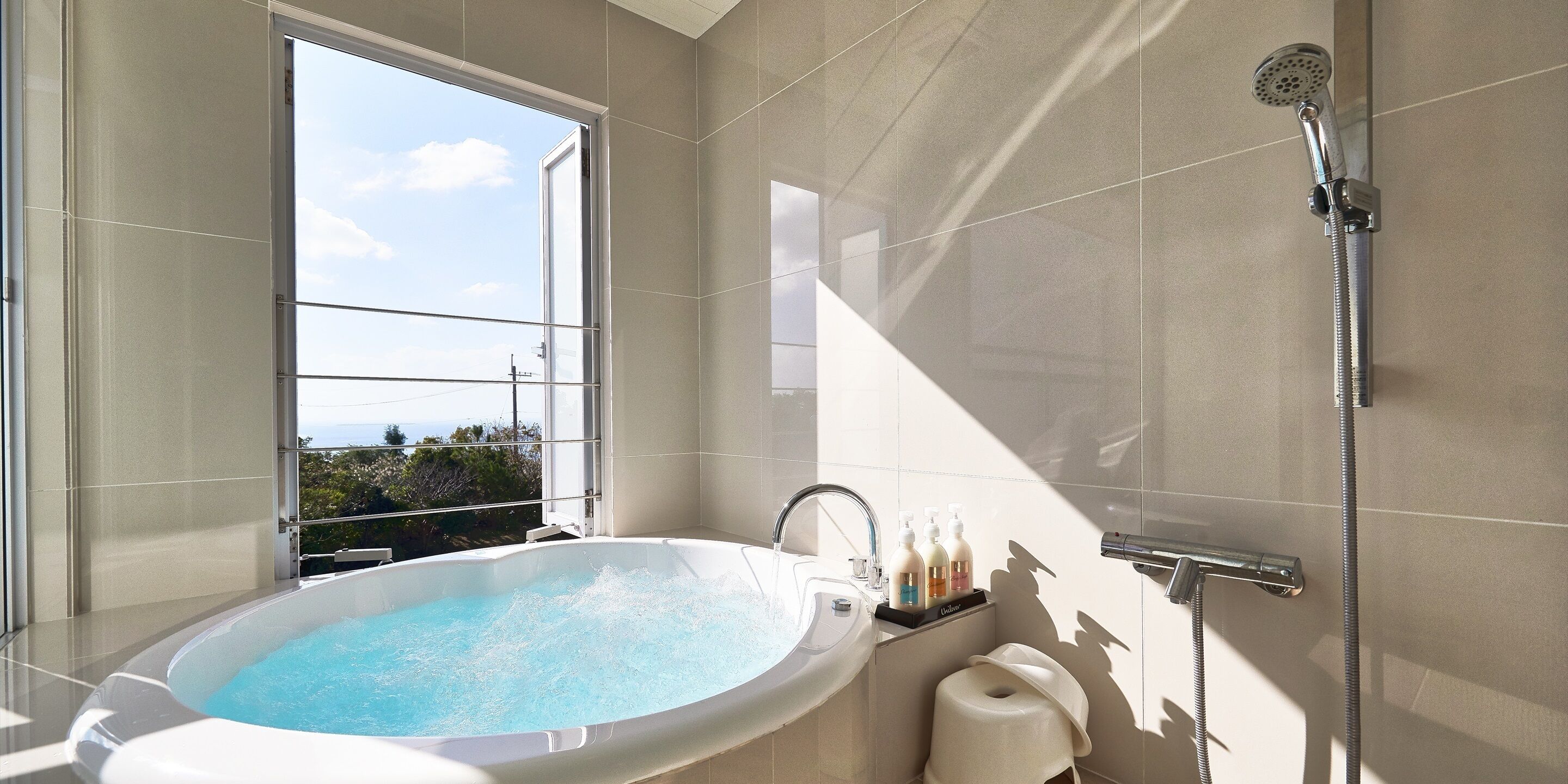 Une salle de bain moderne dotée d’une grande baignoire, d’une douche et d’une fenêtre offrant une vue sur l’extérieur.