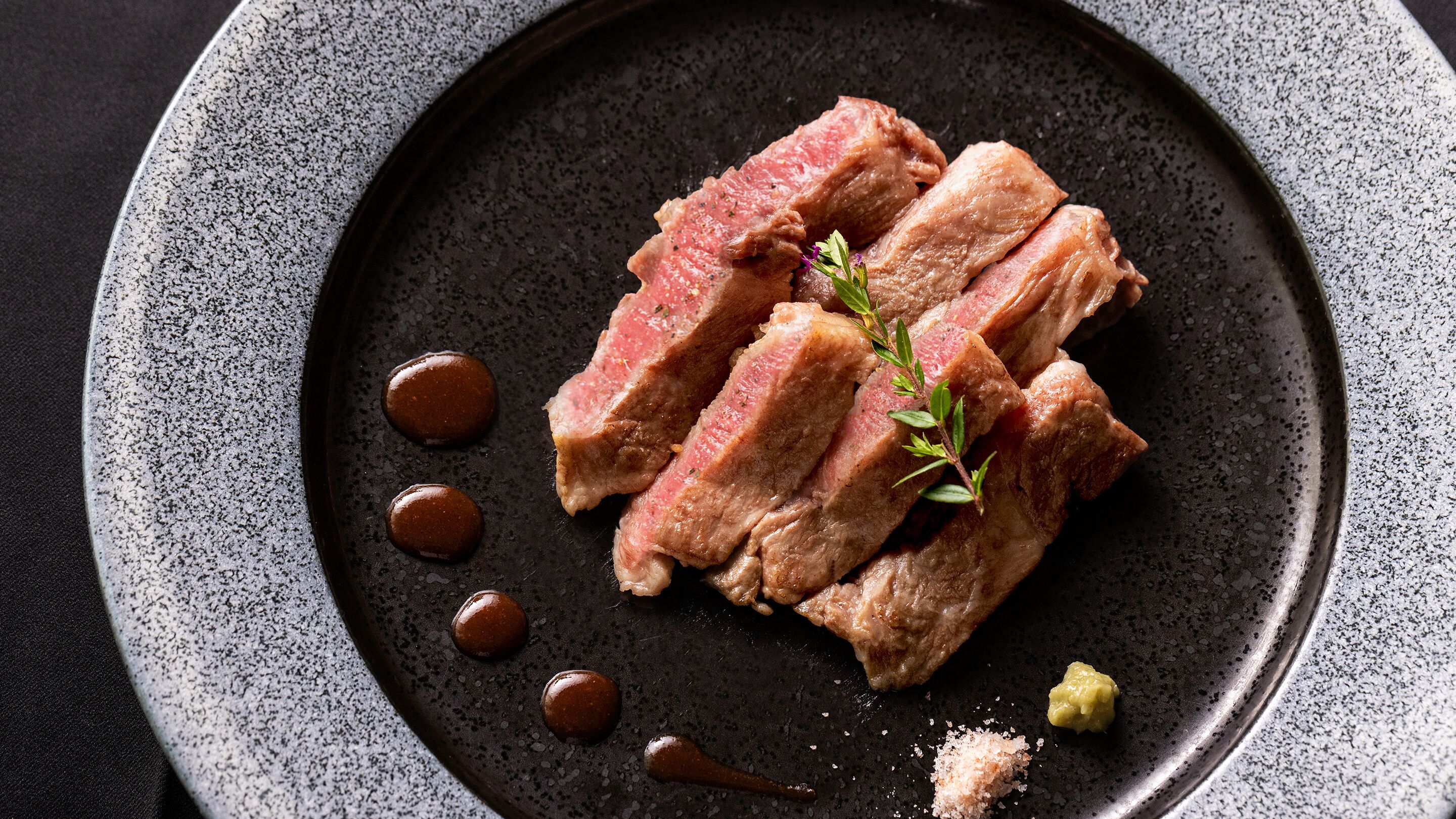 Un plato con carne en rodajas, una ramita de hierbas y dos cucharadas de salsa.