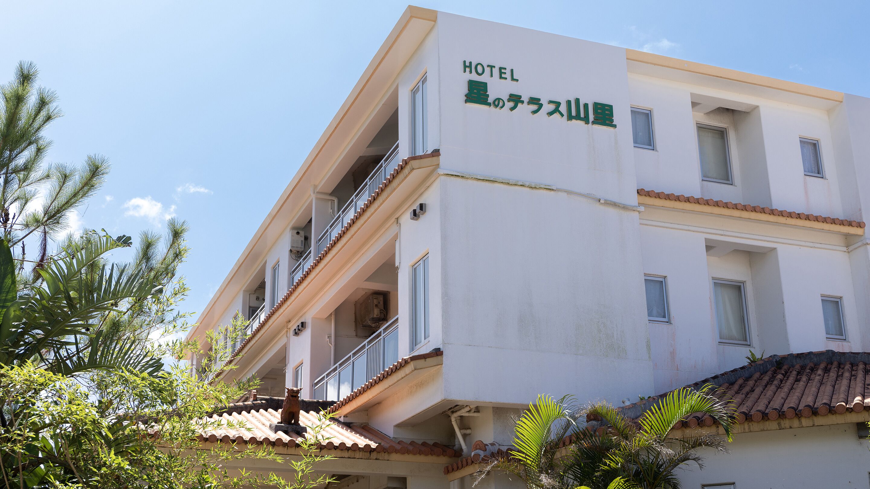 Een hotel met een bord in Japanse schrift, balkons en een pannendak.