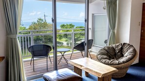 Un balcón con vistas al océano, una silla de mimbre, una mesa de madera y un banco acolchado.