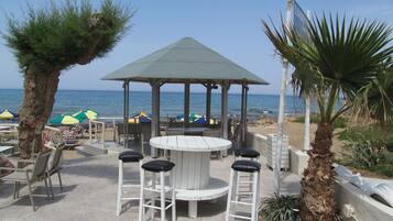 Un patio frente a la playa con un pabellón, mobiliario exterior y vistas al océano.