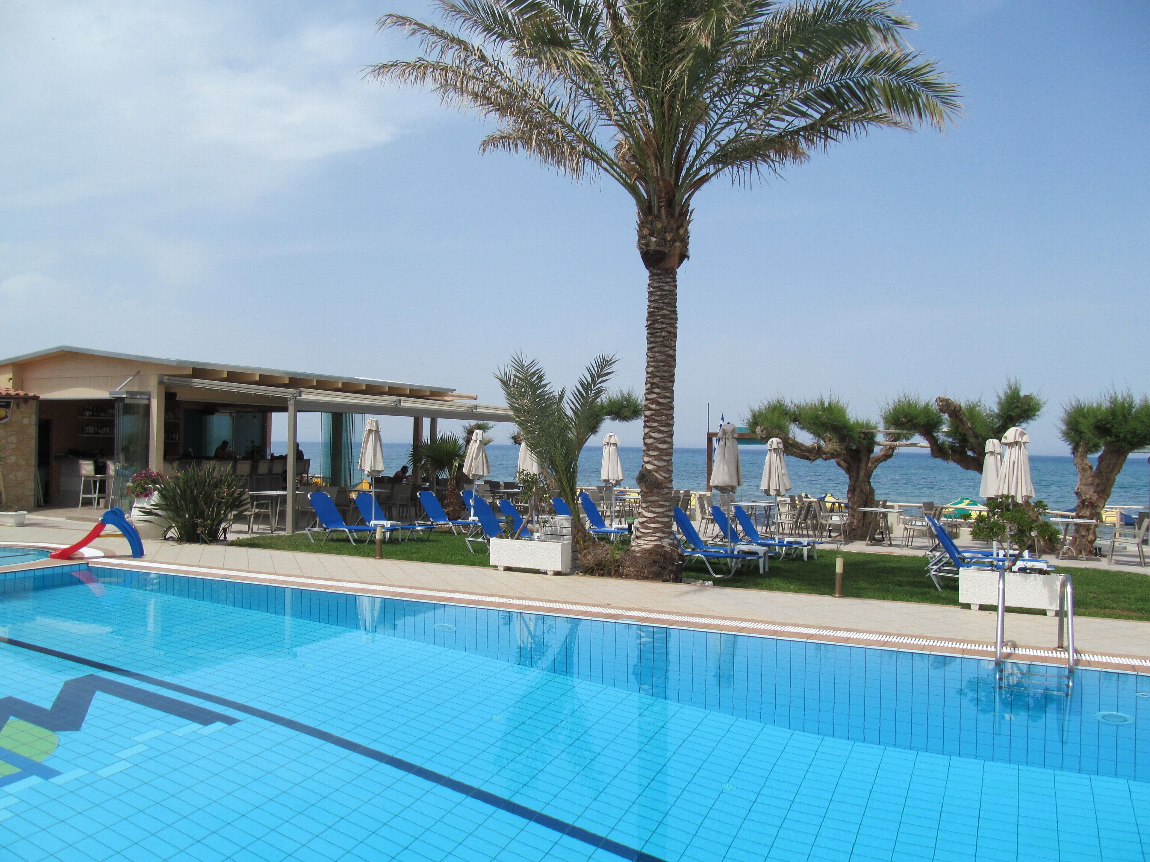 Zona de piscina amb rajoles blaves, seients de relax i ombrelles.