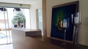 A reception area with a modern counter, a glass door leading outside, and a painting on the wall. - Malliotakis Beach Hotel by Checkin (Hersonissos)